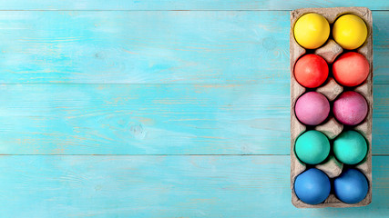 Easter concept. Colorful eggs in cardboard packaging on blue wooden background with copy space for text. Top down view or flat lay. Banner