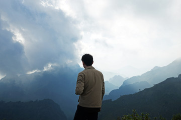 Fototapeta premium A man standing on the peak looking at green mountain range with cloudy sky
