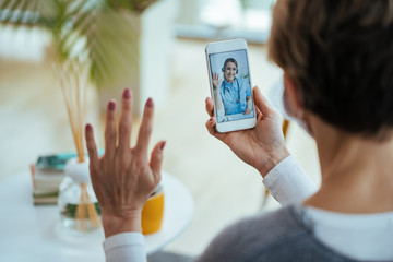 Happy doctor waving while having video call with patient over mobile phone. - obrazy, fototapety, plakaty