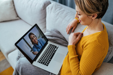 Woman using laptop and having video call with her doctor while sitting at home. - obrazy, fototapety, plakaty