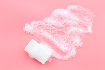 Soap bar with foam on pink background top-down