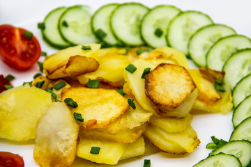 Homemade fried potatoes with fresh cucumbers, cherry tomatoes and sauces on the white plate. Delicious ukrainian fried potatoes with vegetables against background. Cooked tasty meal for lunch.