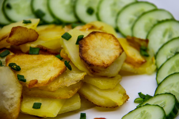 Homemade fried potatoes with fresh cucumbers, cherry tomatoes and sauces on the white plate. Delicious ukrainian fried potatoes with vegetables against background. Cooked tasty meal for lunch.