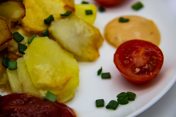 Homemade fried potatoes with fresh cucumbers, cherry tomatoes and sauces on the white plate. Delicious ukrainian fried potatoes with vegetables against background. Cooked tasty meal for lunch.