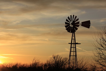 Kansas Windmill silhouette at Sunset with a tree out in the country north of Hutchinson Kansas USA.