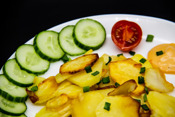 Homemade fried potatoes with fresh cucumbers, cherry tomatoes and sauces on the white plate. Delicious ukrainian fried potatoes with vegetables against background. Cooked tasty meal for lunch.