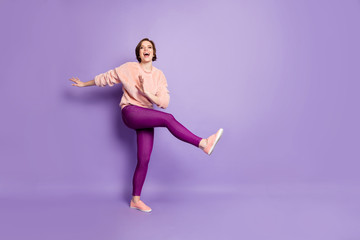 Fototapeta na wymiar Full size photo of pretty lady dancing strange modern moves disco party students chilling raise one leg excited wear casual stylish pullover pants isolated purple color background