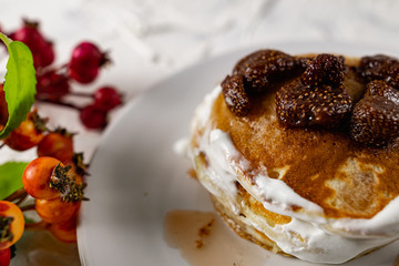 A stack of crumpets and pancakes with sour cream and strawberry sweet jam with berries on top of the dish. Dessert on a white plate with fruit in the background.