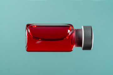 Medical or vaccine vial for injection with red liquid, macro on a blue background