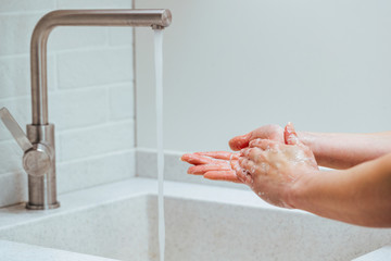 Close-up of woman washing hands with soap in the bathroom.