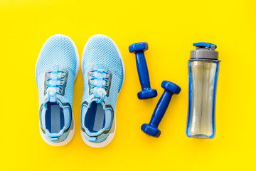 Sport equipment. Sneakers, dumbbells and water on yellow table top view