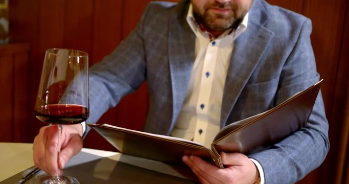 male guest of restaurant is choosing meal in menu and enjoying expensive red wine