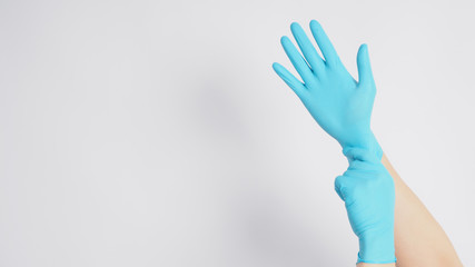 Hand is pulling blue latex gloves on white background.