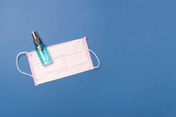Medical face mask and sanitizer on blue background with copy space