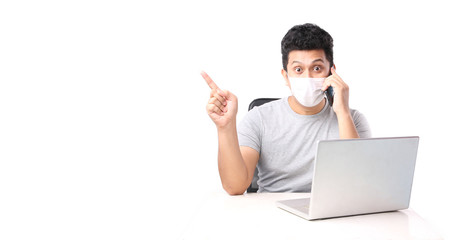 handsome man wearing a mask is sick Pointing finger holding mobile phone That has The computer page in front of. on white background in studio With copy space.Concept work from home covid-19