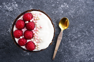 top view dessert with raspberries and cream mousse in coconut bowl with spoon on gray background