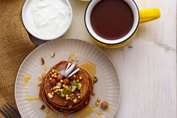 chocolate pancakes with kiwi, hazelnut, honey on plate with sour cream and cup of cocoa on white background