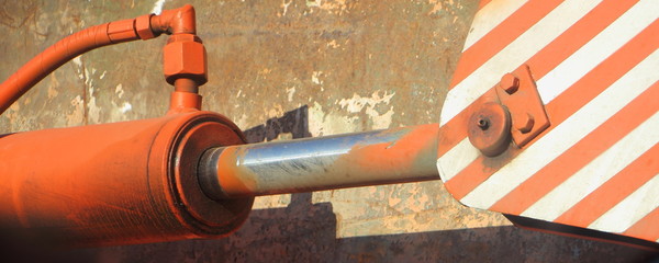 Old painted orange hydraulic cylinder of special equipment close up