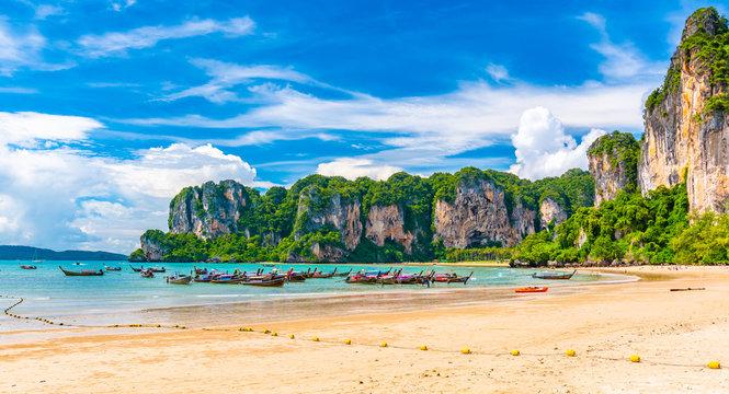 Beautiful view of long tail boats on water in Railay beach bay, Thailand, Krabi town. Famous tourist destination for vacation in tropical paradise. Beautiful summer day. Big limestone hill and rock