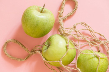 Zero waste concept - environmental care. String bag with green apples on a pink background.