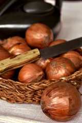 Brown onions in a wicker basket with old rustic kitchen knife closeup. Healthy food concept. Vertical, selective focus.