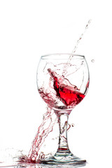Splash of falling red wine in a round glass on a white background