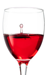 Splash from a drop of falling red wine to the surface in a round glass on a white background