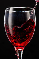 Splash of falling red wine in a round glass on a black background