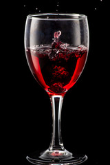 Splash of falling red wine in a round glass on a black background