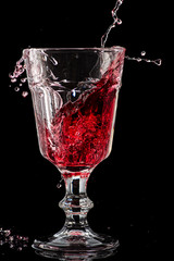 Splash of falling red wine in a round glass on a black background