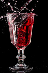 Splash of falling red wine in a round glass on a black background