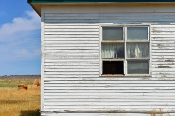 Torn curtains in the windows of an abandoned white building on the Montana prairie