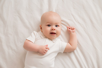 Healthy toddler boy smiling in white clothes lies on the bed view from above