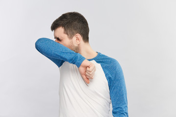 bearded man in blue and white shirt sneezing in his elbow to protect others from coronavirus