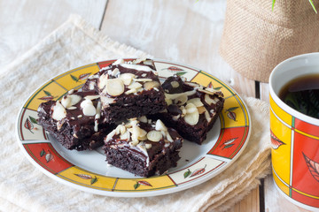 Closed-up of homemade chocolate brownies with almond nuts and white chocolate chips topping on white wooden background.
