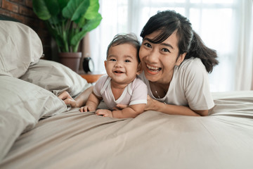 Fototapeta premium happy asian mother playing together with her baby on the bed