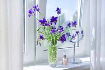 Close up of beautiful blue purple irises in a vase, perfume, make-up mirror on the window