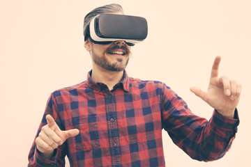 Content man using virtual reality headset. Cheerful bearded man in checkered shirt moving hands and using VR headset on grey background. Technology concept