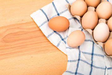 chicken eggs in an open cardboard box on a wooden table with a cotton towel.