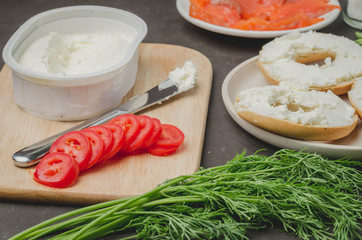 cooking of a food with round toast with cheese, red fish, tomatoes and vegetables on black table/Healthy food with round toast, red fish, vegetables and cheese on black table.