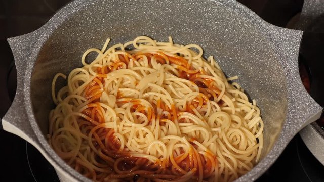 Cooking and stirring the spaghetti with red tomato sauce in the frying pan, close-up slow motion