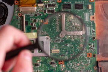 laptop motherboard chip through a magnifier glass. Laptop repair service