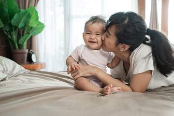 happy asian mother playing together with her baby on the bed