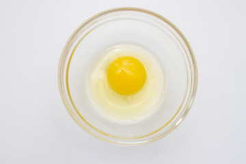 raw chicken egg with yolk in a transparent bowl on a white table