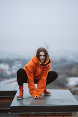 Girl in an orange jacket poses on the roof of a building in the city center