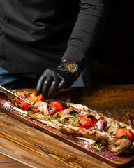 the chef cuts tomatoes, meat on a ramrod with onions and herbs in pita bread