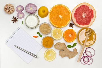 Set of products of citrus, ginger, honey, garlic, onions yogurt. Notebook and pen on table.