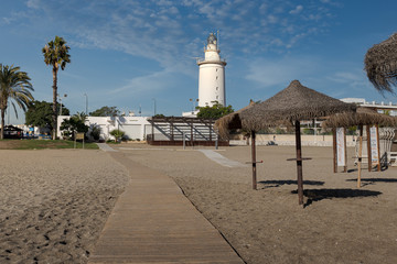 Malagueta Beach with straw beach umbrellas and Lighthouse.