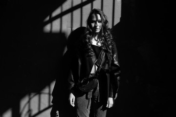 Fototapeta na wymiar Outdoor portrait of a young woman in hard light with shadows of urban wearing trendy black jacket with incredible makeup. Black and white photography. Text space.