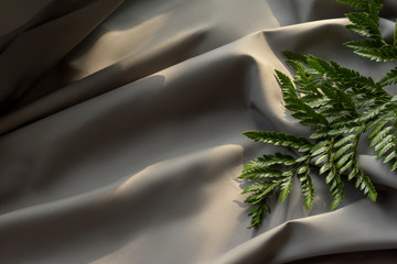 silk fabric texture, bed linen in gray, green leaf on the bed